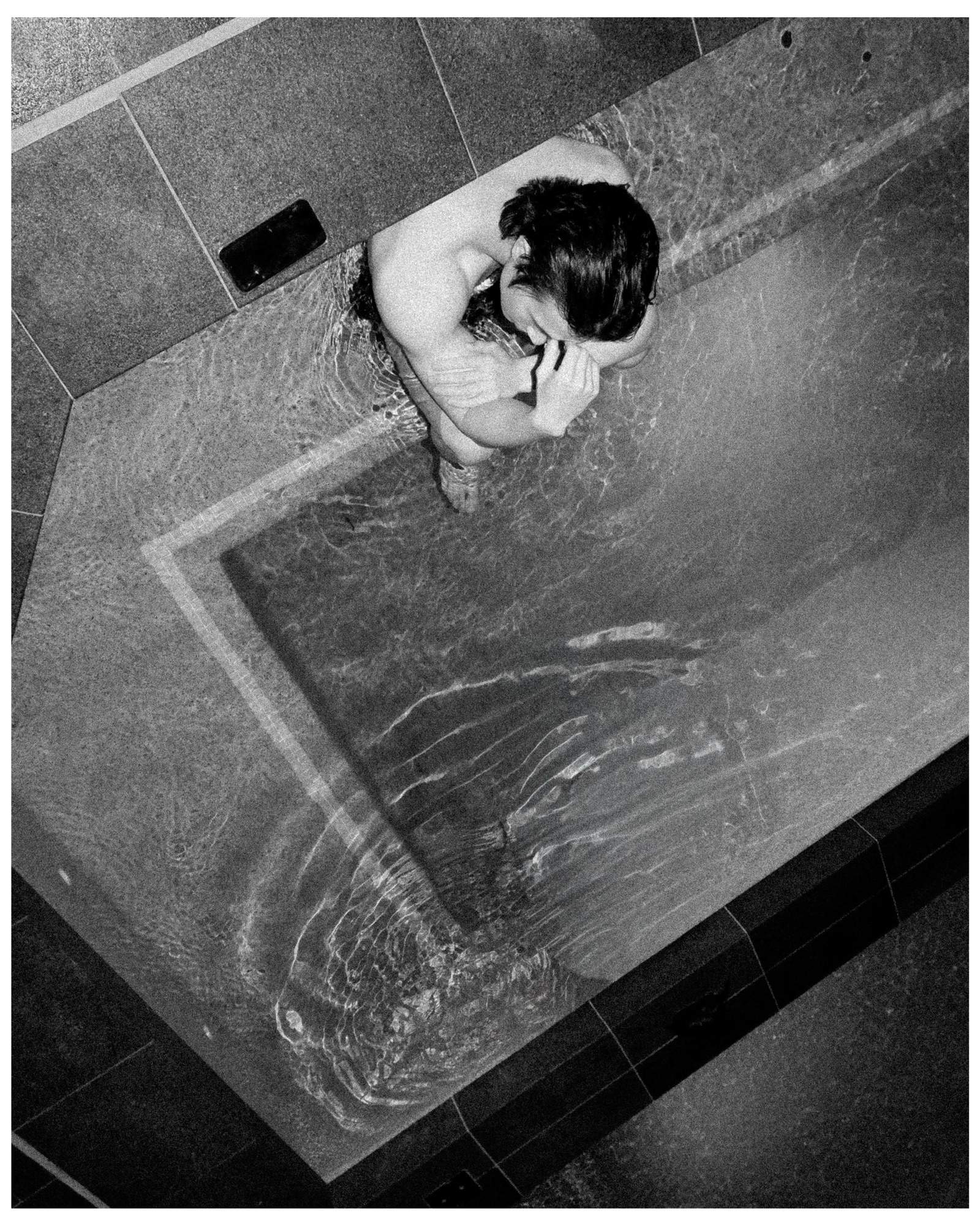 Figure in a bathtub from above, black and white, glassy water surface
